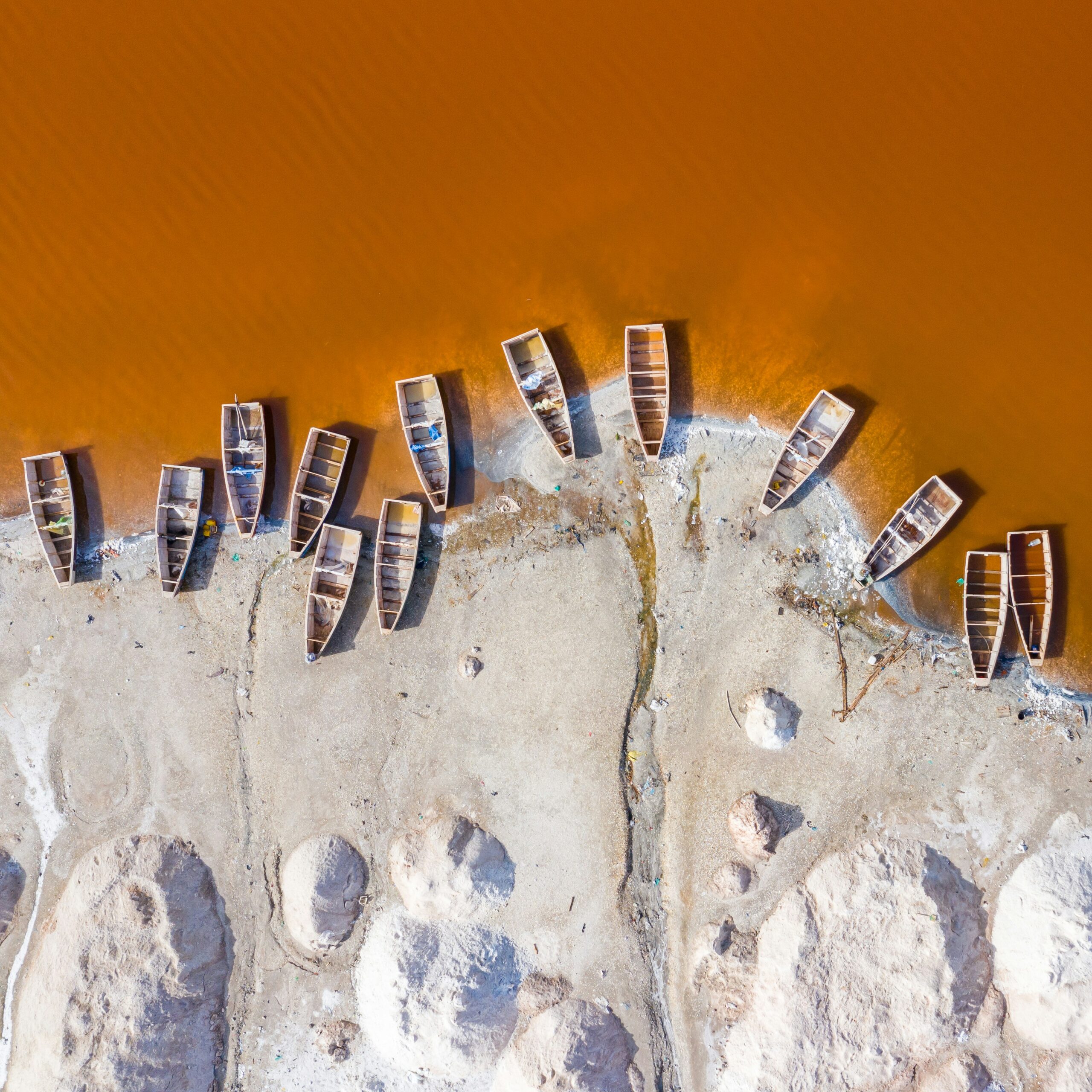 This image shows an aerial view of Lac Rose in Senegal. Boats are docked at the shore. 